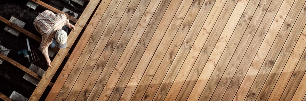 Personne installant des planches de bois clair rainurées pour une terrasse en construction. Vue d'en haut sur le chantier du deck.