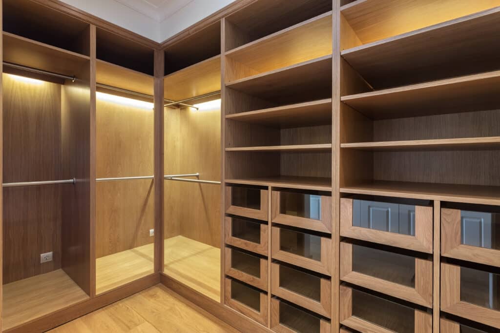 Grand dressing en bois clair sur mesure avec étagères ouvertes, barres de suspension, tiroirs vitrés et éclairage LED intégré.