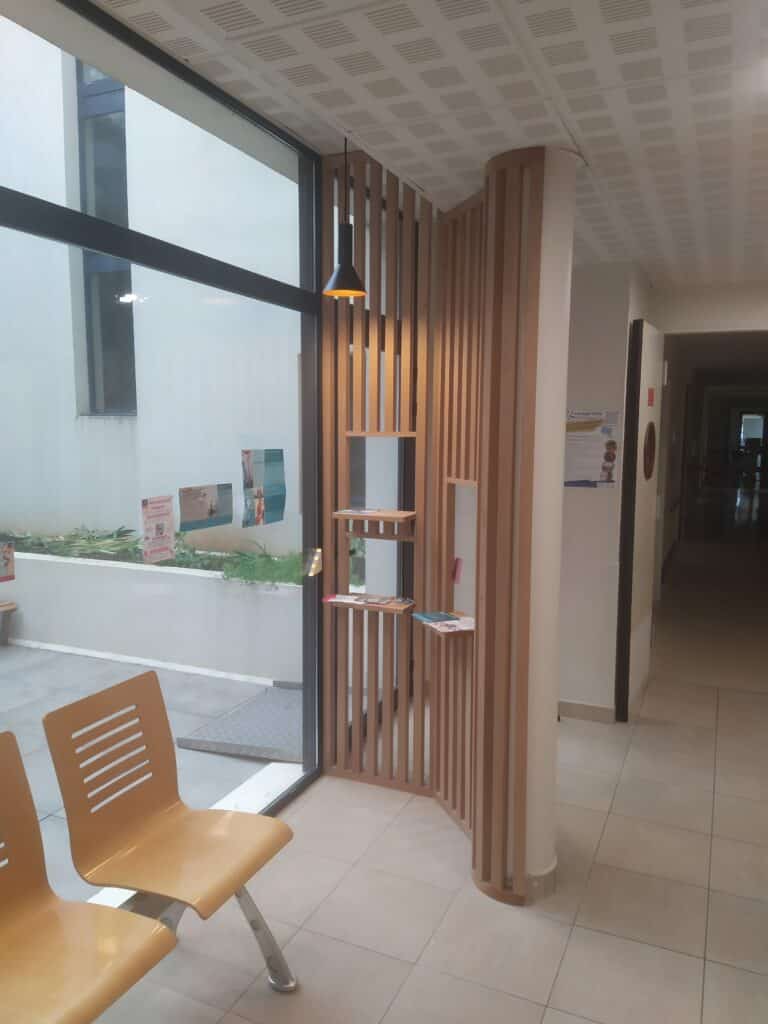 Salle d'attente moderne – Design bois, lumière et infos. Salle d'attente moderne et lumineuse avec fenêtres, chaises orange, cloison en bois, brochures d'info et affiche #seeph2024.