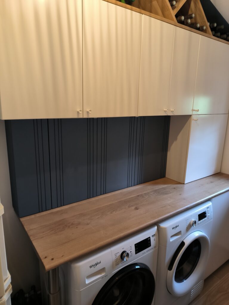 Buanderie moderne : Rangement, bois clair et Whirlpool Buanderie moderne avec comptoir en bois clair, placards blancs, panneau arrière bleu-gris rainuré et deux appareils Whirlpool superposés.