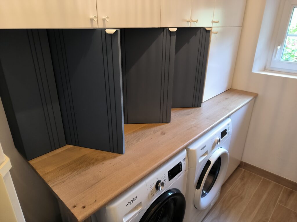 Buanderie moderne : Rangement et électroménager intégré Buanderie moderne avec plan de travail en bois clair recouvrant des lave-linge Whirlpool et des placards bas gris anthracite sous des meubles hauts blancs à poignées rondes.