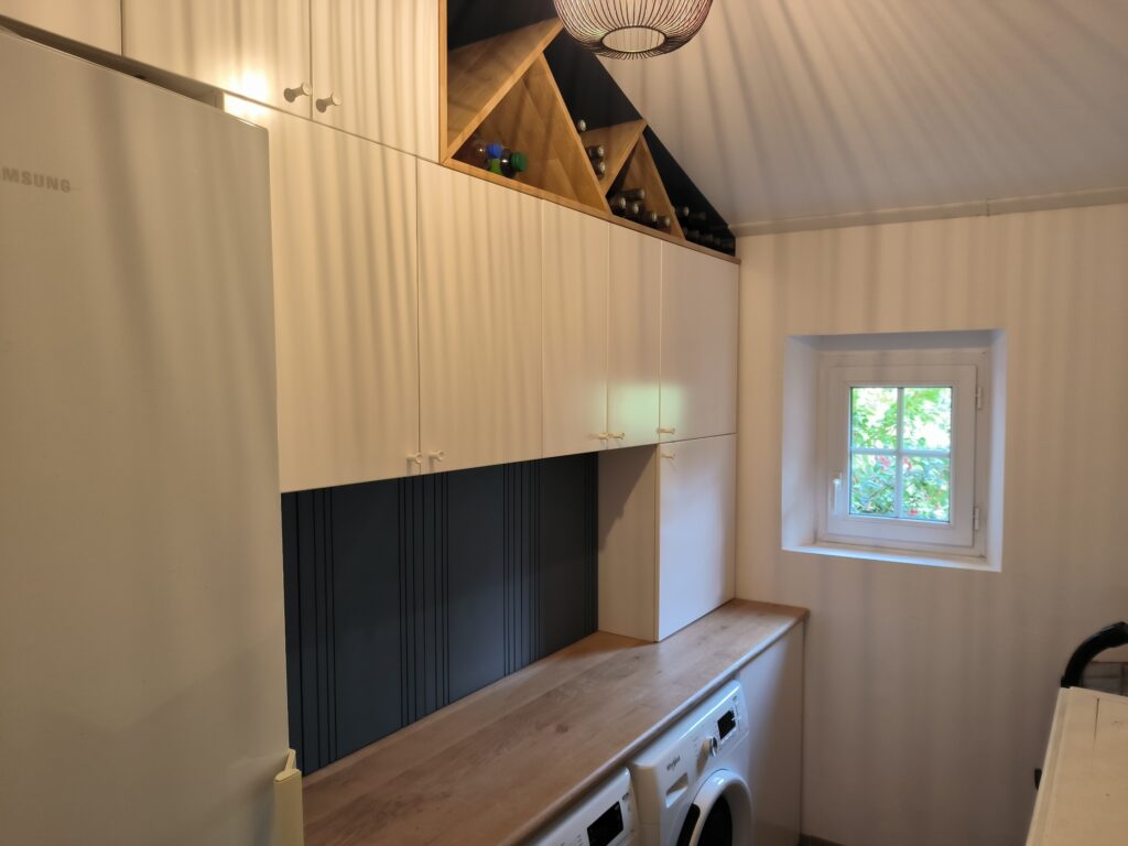 Buanderie moderne : Rangement, bois et coin machine Buanderie moderne avec rangements blancs, plan de travail en bois, lave-linge Samsung et étagère à vin inclinée sous plafond mansardé.