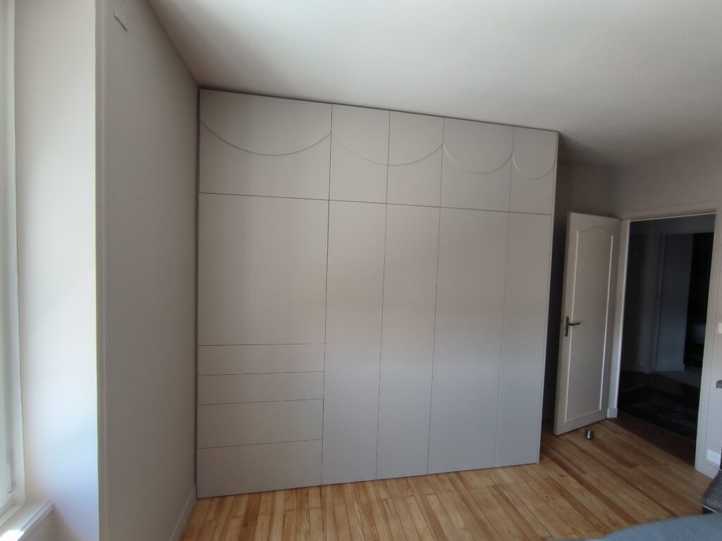 Armoire sur mesure beige clair du sol au plafond avec tiroirs et détails circulaires sur parquet en bois clair.